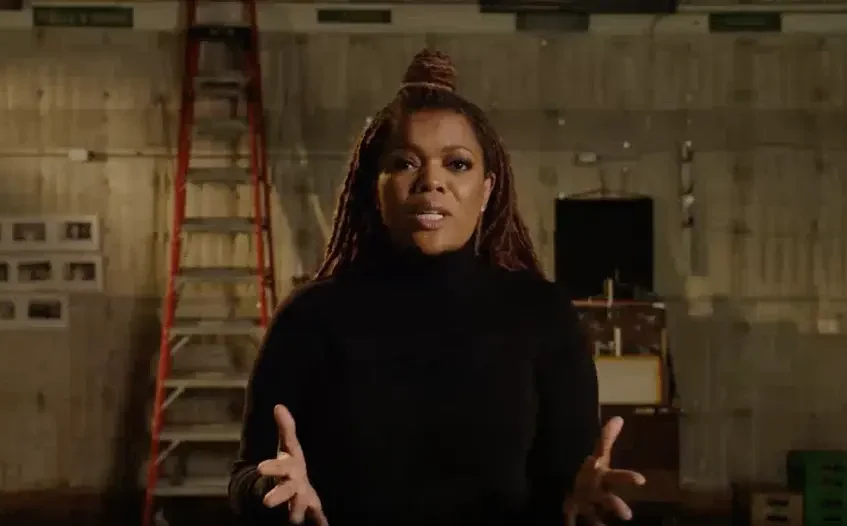 A still from the Caregivers Don't Wear Capes video, with Yvette Nicole Brown addressing the camera while standing backstage on a film set.