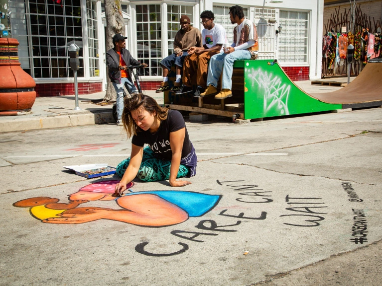 An artist adds finishing touches to a pavement drawing that reads 