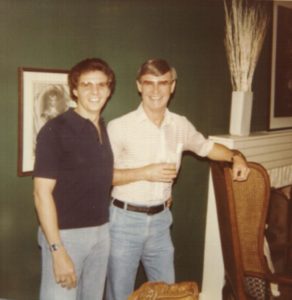 Dr. Cheryl Morris's father and Rick standing together in the living room with a green wall behind them.