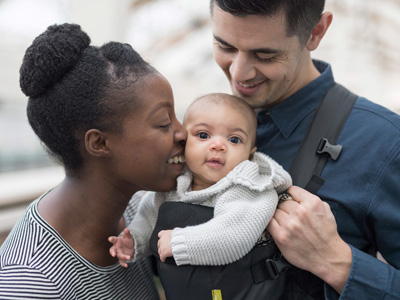Two parents of different races hold and smile at a baby in their arms.