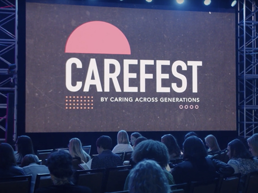The audience at CareFest looks at a large screen with the CareFest logo projected upon it.