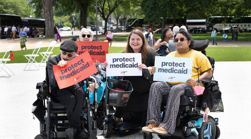 Four people in wheelchairs hold signs reading