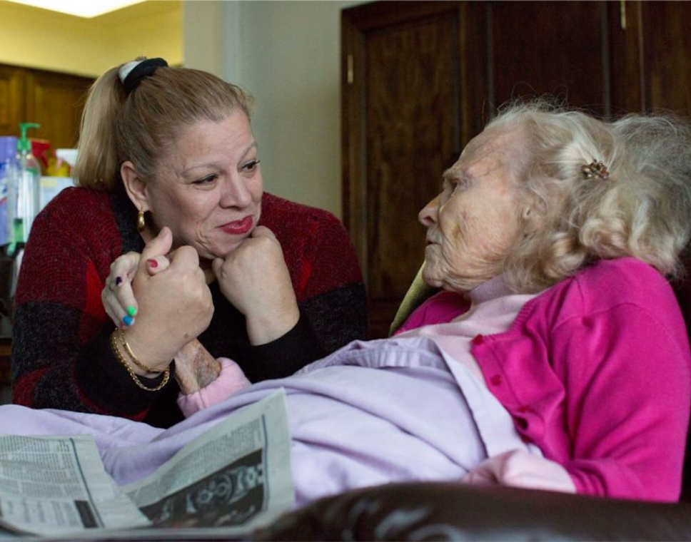 A woman holding an elderly woman's hand while in a nursing home.