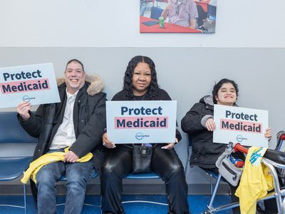 Three people sit on chairs, holding signs that say