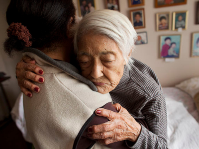 A photo of an elderly woman being assisted by a caregiver to get out of bed.